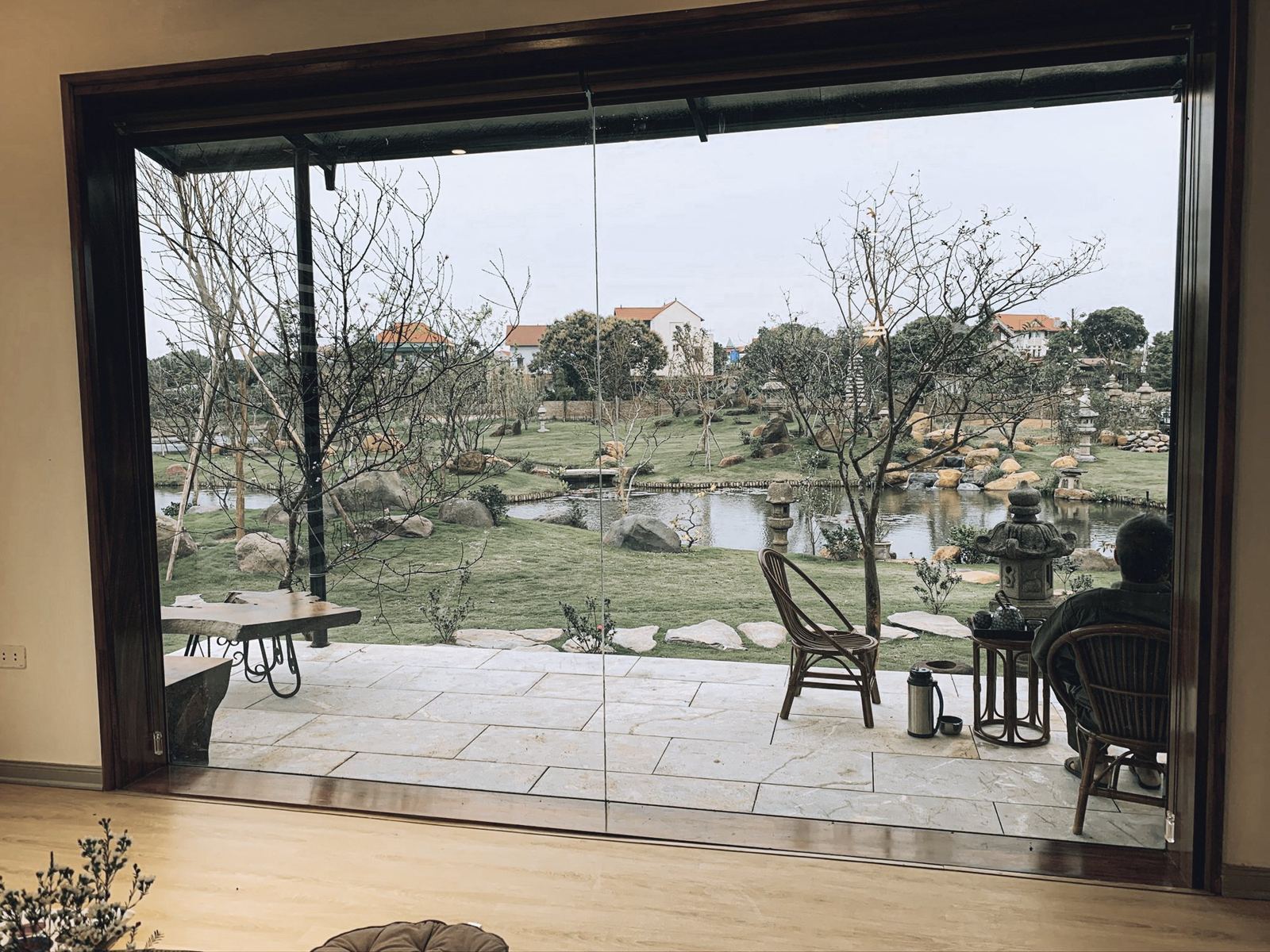 Một người ngồi ghế mây trong hiên nhà nhìn ra vườn